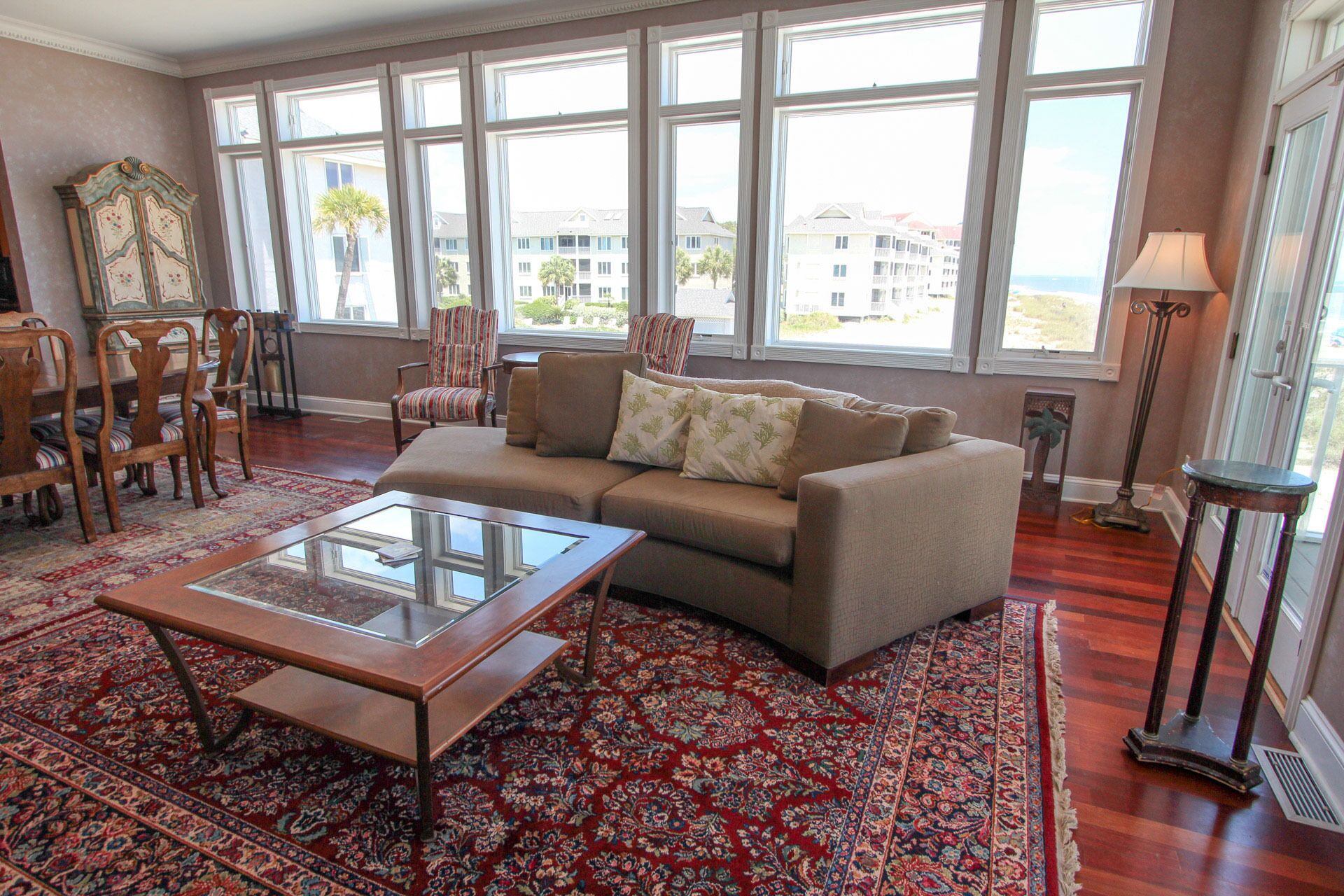 A living room with a sofa, armchairs, a glass coffee table, and a patterned rug.
