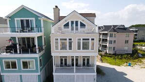 A beachfront property with a two-story building featuring balconies, a covered patio, and a sandy beach area. - Three story home with sweeping ocean views and game room in Wild Dunes (Isle of Palms)