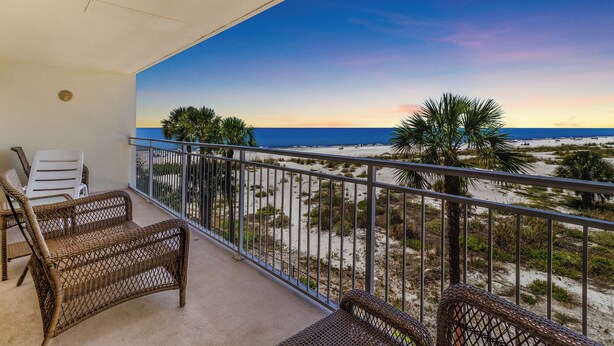 A balcony with wicker furniture, a view of the beach, and a clear sky.