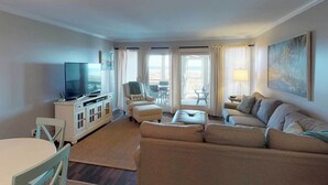 Ein Wohnzimmer mit einer Couch, Sesseln, einem Fernseher und einem Essbereich mit Tisch und Stühlen.