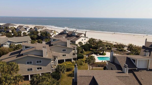 A residential area with houses, a swimming pool, and a beach in the background.