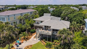 A multi-story house with a balcony, surrounded by lush greenery and palm trees.