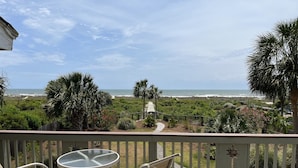 A deck with two chairs and a table, overlooking a beach and a path leading to the ocean.