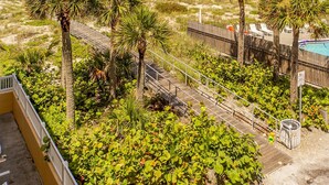 A beach view with palm trees, a wooden deck, and a clear sky. - Beach View 1b 1b - Balcony - King - Surf Song #346 (Madeira Beach)