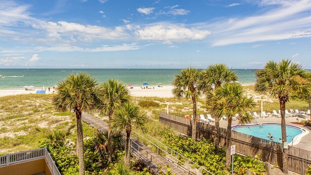 A beach resort with a pool, palm trees, and a view of the ocean. - Beach View 1b 1b - Balcony - King - Surf Song #346 (Madeira Beach)