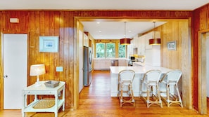 A kitchen with wooden paneling, a central island with bar stools, and a view through the window. - Oceanfront beach home-large screened porch, rooftop deck, beach access! (Isle of Palms)