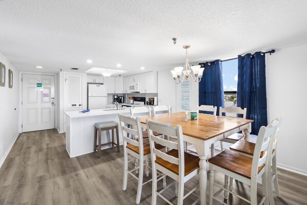A modern kitchen with white cabinets, a central island, and a dining area with wooden chairs and a table.