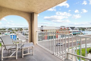 A balcony with two striped chairs, a view of a street with a building labeled 'Bubba Gump's' in the background.