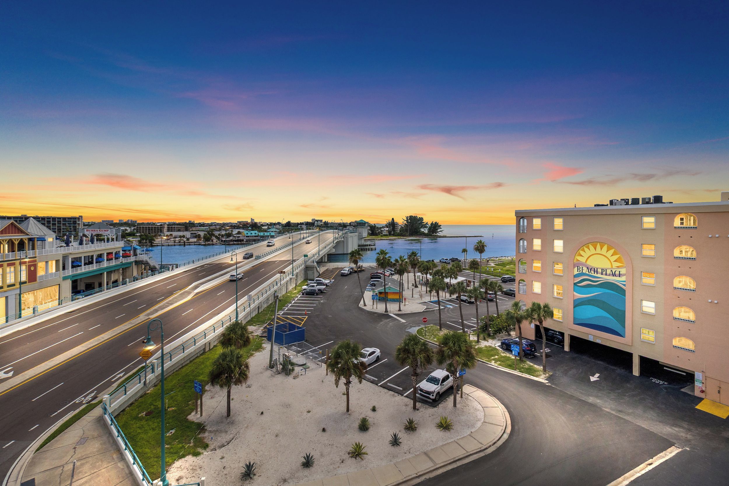 Un paisaje urbano costero con un edificio destacado que presenta un mural con temática marina, una carretera con varios carriles y un puerto deportivo.
