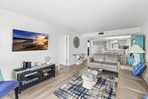 A modern living room with a flat-screen TV, a sofa, a coffee table, and a dining area with a chandelier.