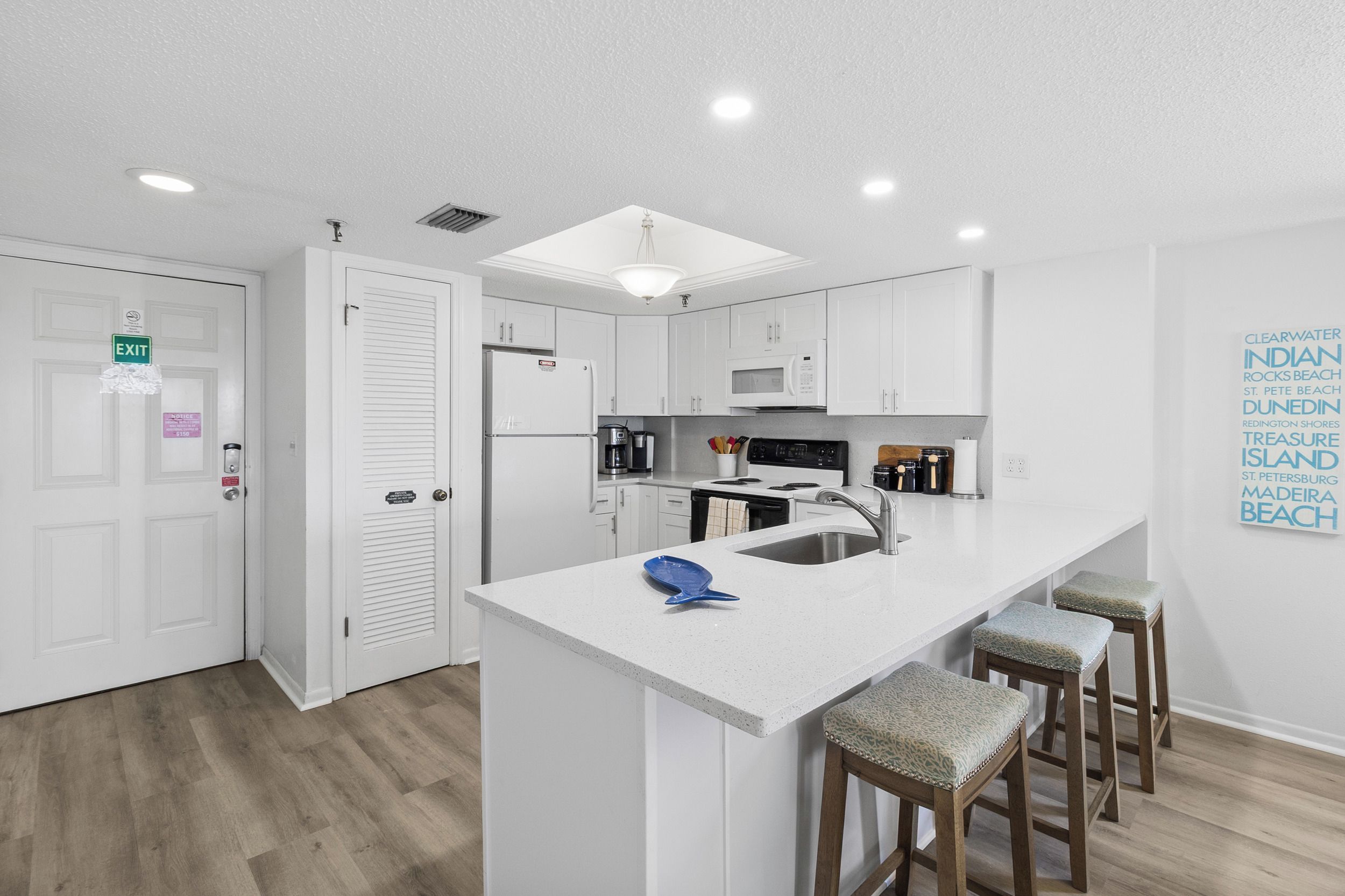 A modern kitchen with white cabinetry, a central island with stools, a microwave, and a refrigerator.