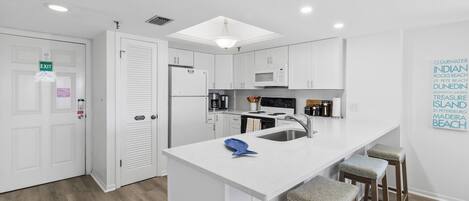 A modern kitchen with white cabinetry, a central island with stools, a microwave, and a refrigerator.