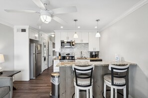 A modern kitchen with white cabinets, stainless steel appliances, a herringbone backsplash, and a bar area with two stools. - Welcome to Your Oceanfront Oasis with Private Balcony! (Isle of Palms)