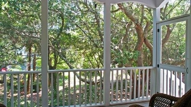 A covered porch with white railings, wicker chairs, and a view of trees. - Beautifully decorated and spacious home in Wild Dunes with a private pool (Isle of Palms)