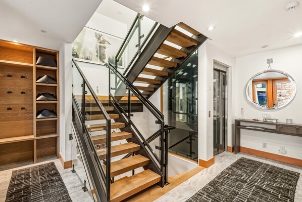 Un escalier moderne avec des marches en bois et des rampes en verre, menant à un deuxième étage.