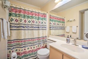 Un bagno con tenda da doccia decorata, un water, un lavandino con dispenser di sapone e uno specchio.