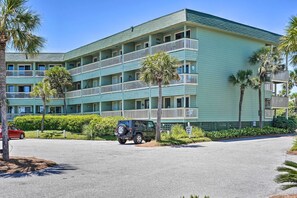 Un hotel a più piani con balconi, palme e un SUV parcheggiato.