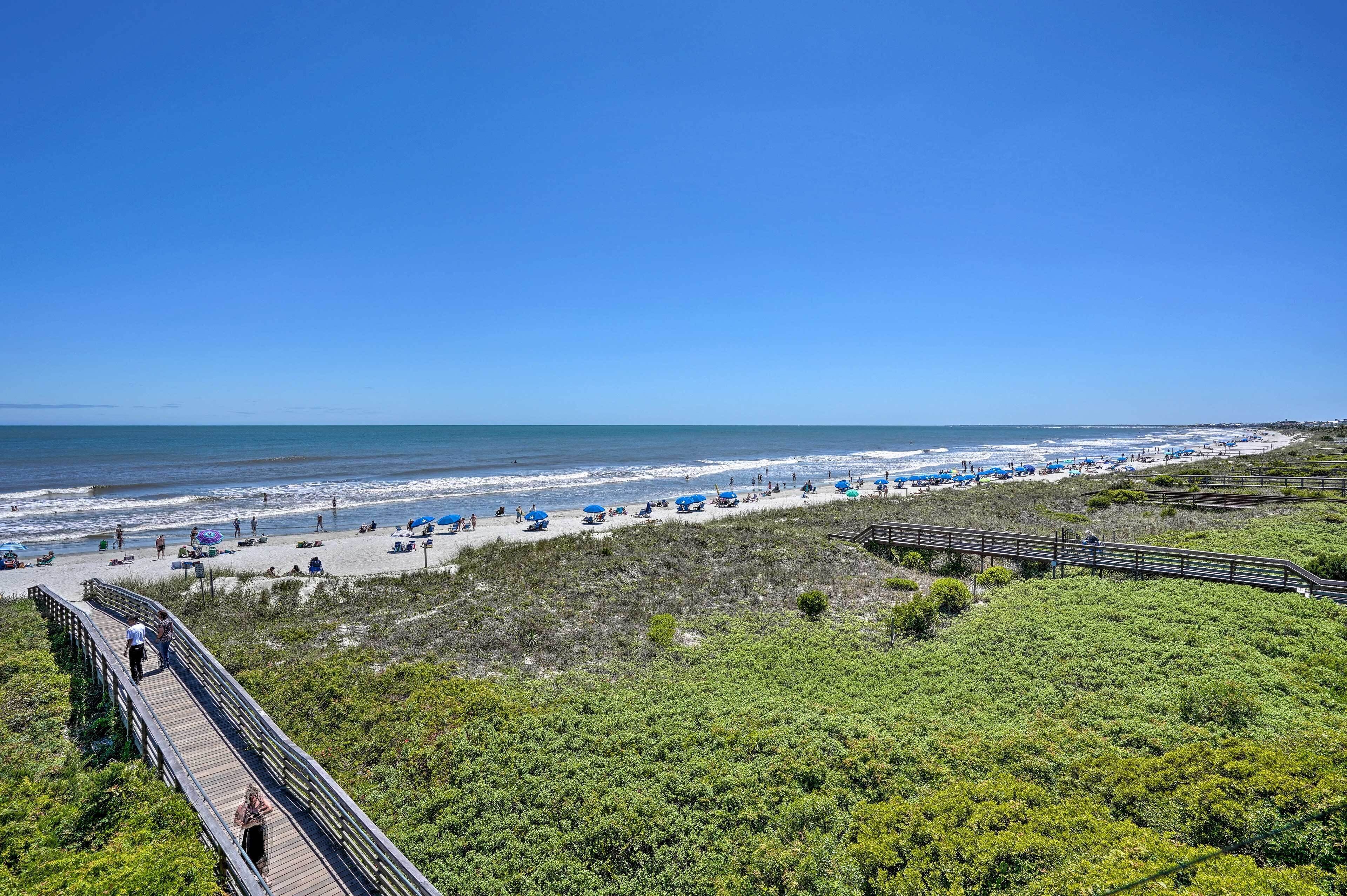 A beach with a wooden boardwalk, beach umbrellas, and a clear view of the ocean.