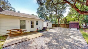 Une maison de plain-pied avec une allée en gravier, un banc en bois et un petit abri de jardin.