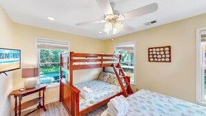 Une chambre avec un lit superposé, un ventilateur de plafond, une horloge murale et un téléviseur affichant le logo « ISLAND REALTY ».