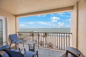 Un balcon donnant sur une plage, avec une balustrade, des chaises et une petite table.