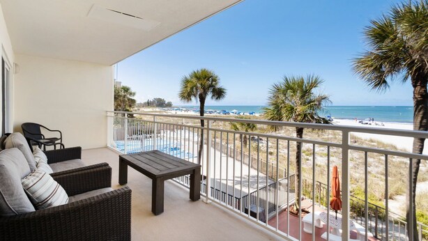 Un balcón con muebles de mimbre, vista a la playa y palmeras.