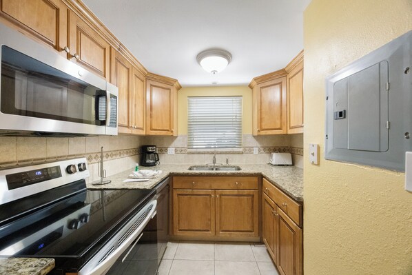 A kitchen with wooden cabinets, a stainless steel oven, a microwave, and a window with blinds.