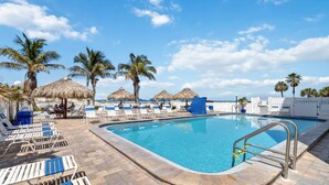 A swimming pool with lounge chairs, palm trees, and thatched umbrellas.