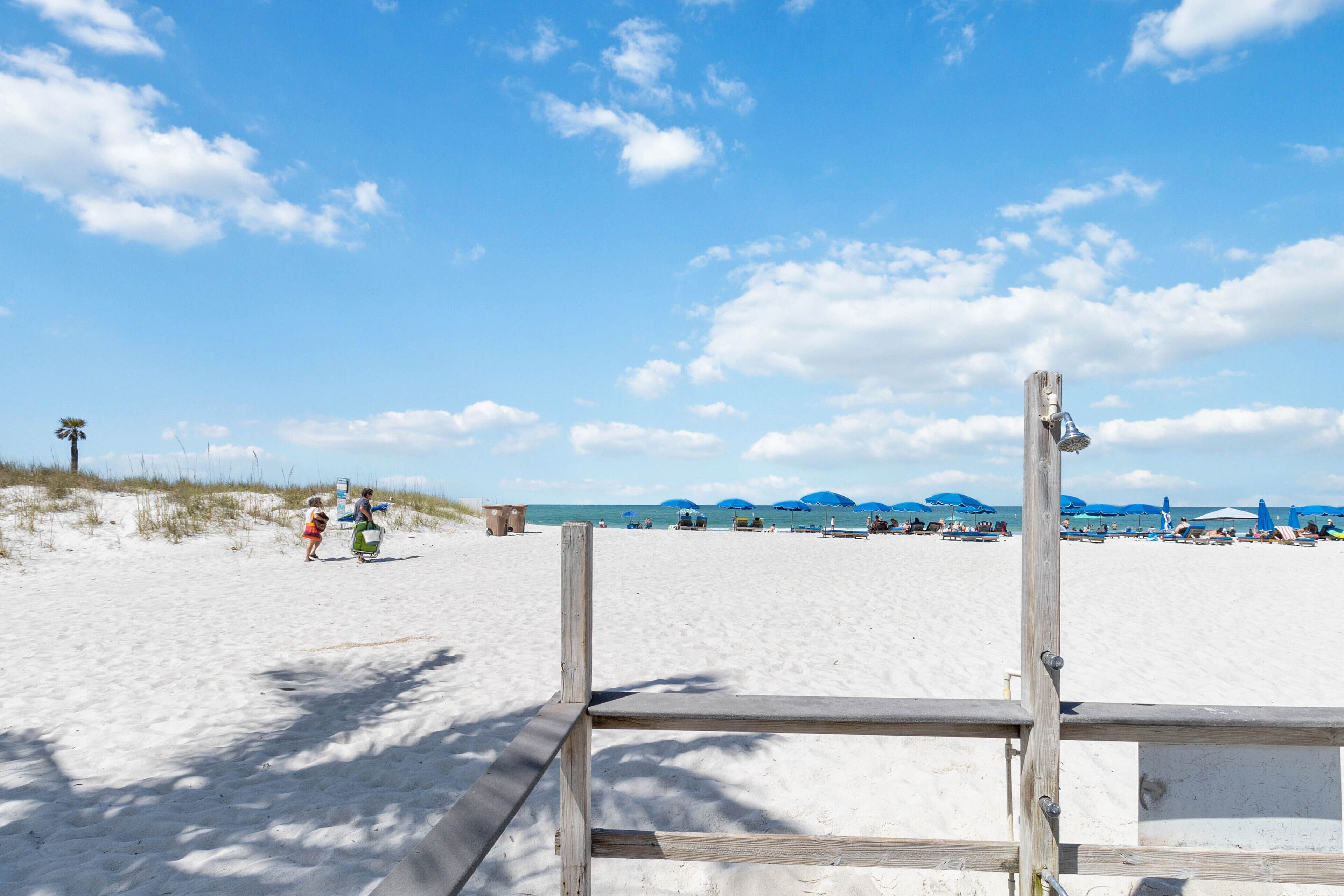 A beach with a wooden fence in the foreground and people in the background.