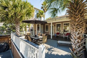 Eine Holzterrasse mit Gartenmöbeln, einer Palme und einem Haus im Hintergrund.