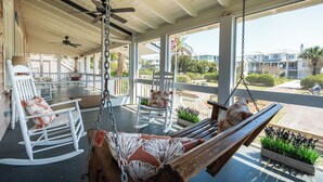 A covered porch with rocking chairs, a hammock, and a view of the surrounding area.