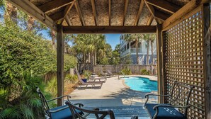 A covered outdoor area with a pool, lounge chairs, and a wooden fence.