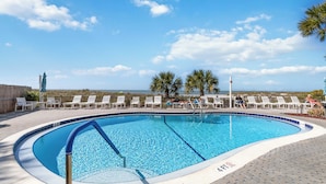Ein Swimmingpool mit Liegestühlen und Blick auf den Strand.