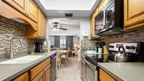 Eine moderne Küche mit Holzschränken, einer Granit-Arbeitsplatte, einem Einbauofen und einem Deckenventilator.