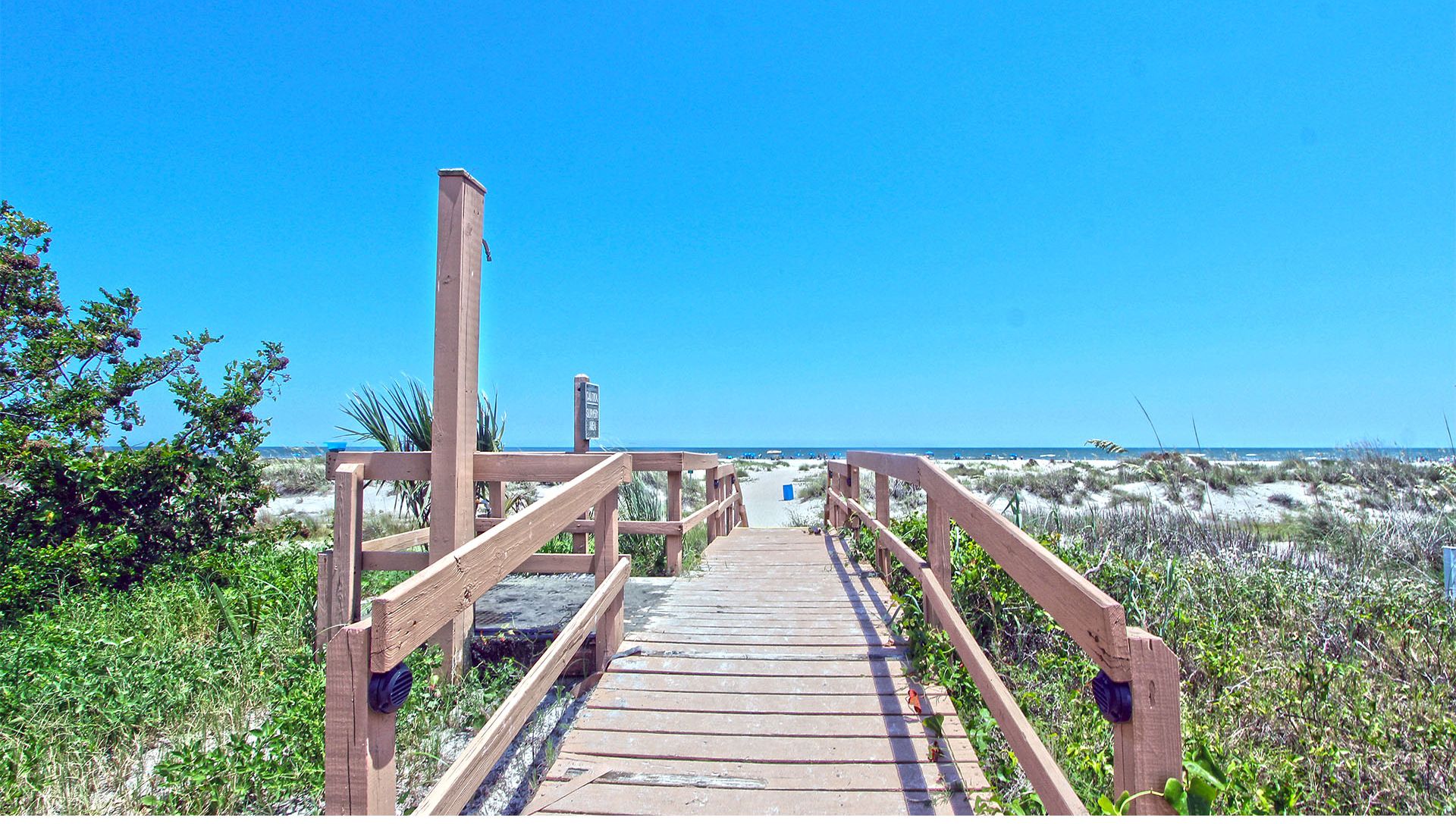 A wooden boardwalk leading to a beach with clear skies.