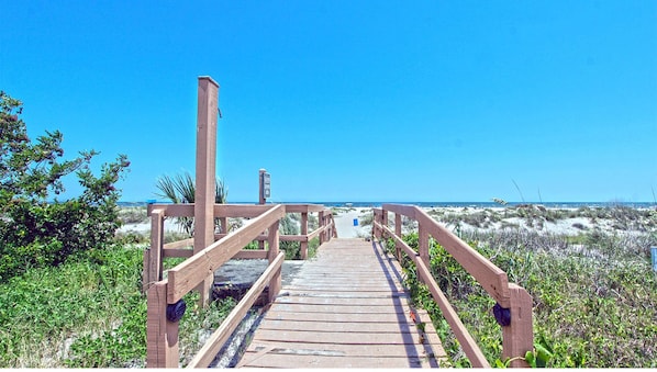 A wooden boardwalk leading to a beach with clear skies.