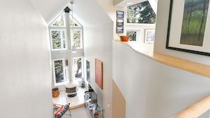 Ein Innenraum mit hohen Decken, einem Kamin, großen Fenstern und Kunstwerken an den Wänden.
