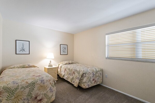 A bedroom with two single beds, a nightstand with a lamp, and a window with blinds. - Best Value, 2nd Floor 2b 2b Near Pool - Surf Song #230 (Madeira Beach)