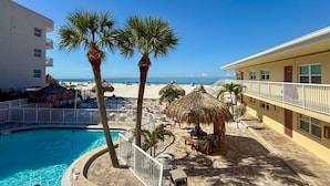 A resort with a swimming pool, palm trees, beach umbrellas, and a view of the ocean. - Best Value, 2nd Floor 2b 2b Near Pool - Surf Song #230 (Madeira Beach)