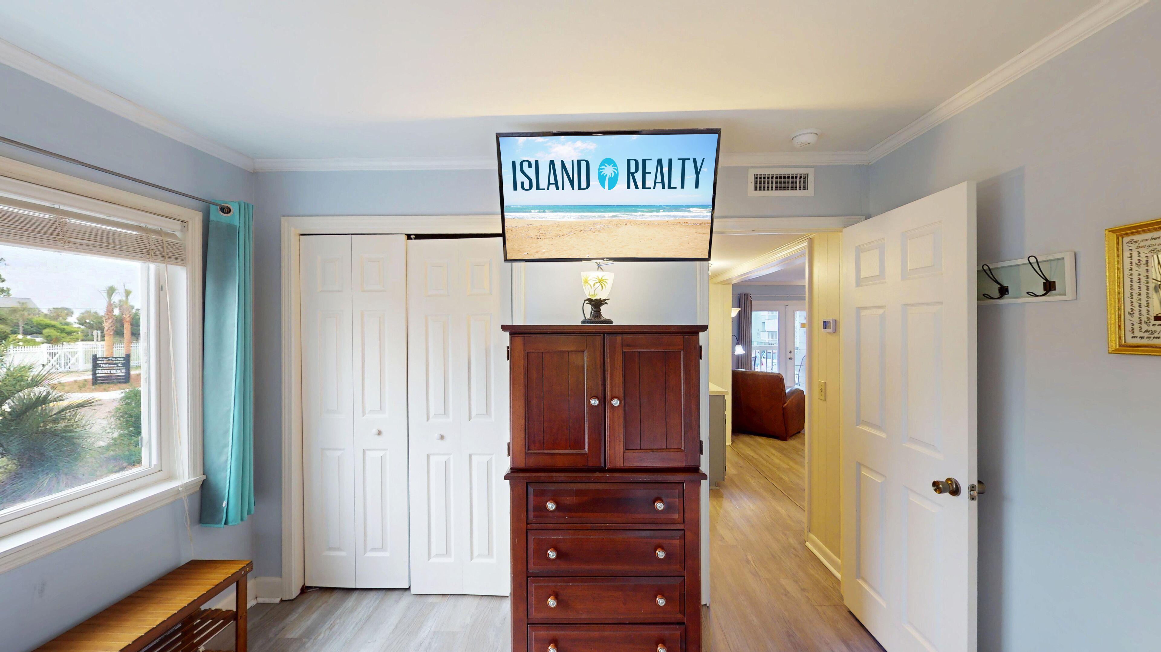 A hallway with a sign reading "Island Realty" above a wooden cabinet. There are white doors, a bench, and a window with blinds.