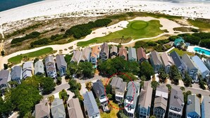 An aerial view of a coastal residential area with houses, a golf course, and a beach.