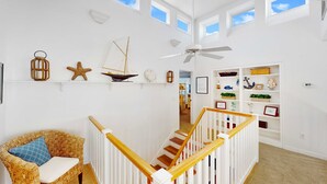 A bright room with a white wall, a wicker chair, a wooden staircase, and a ceiling fan.