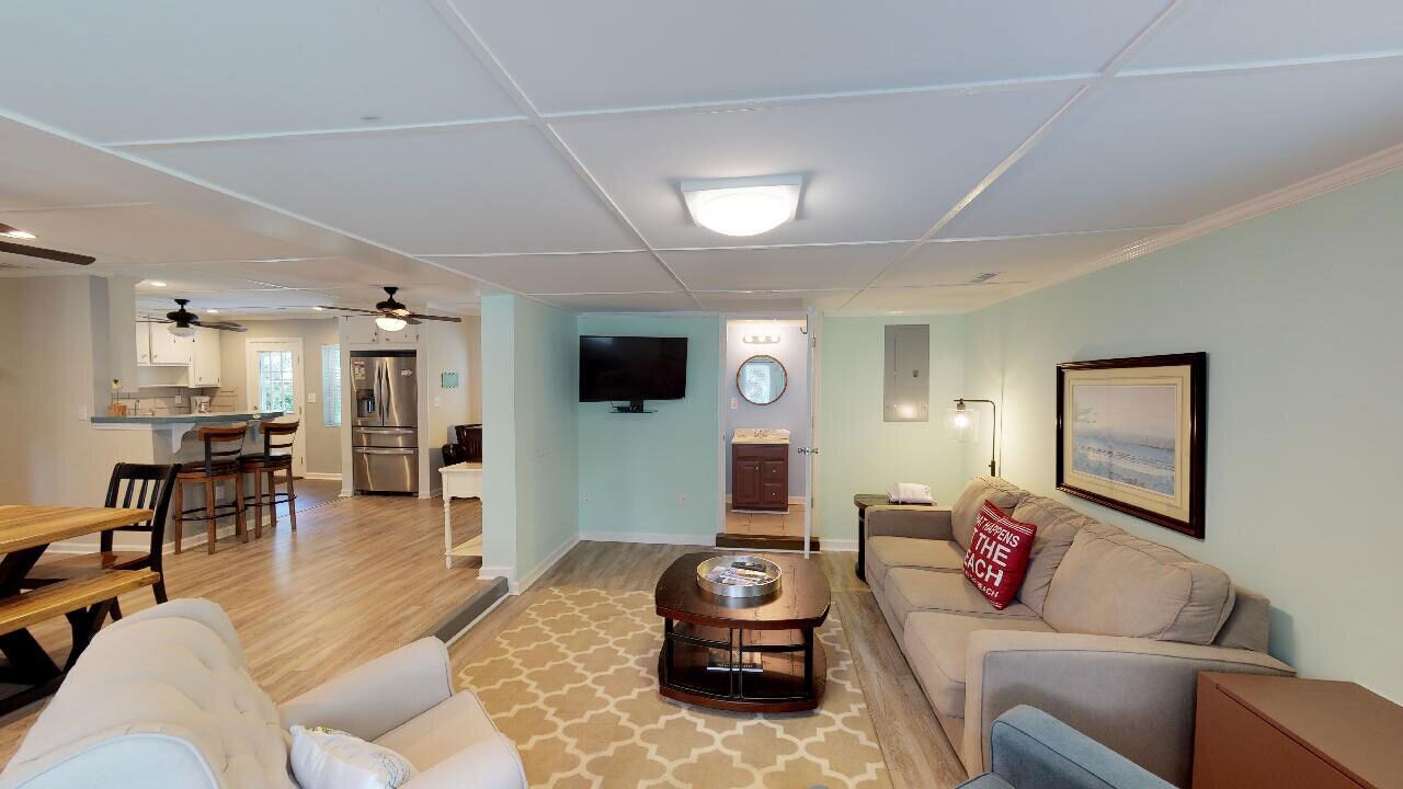 A spacious living room with a sofa, coffee table, and a TV mounted on the wall.