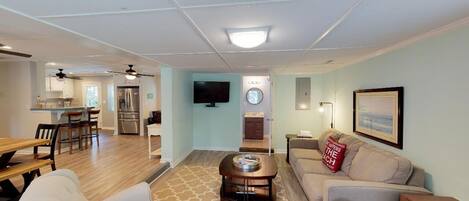 A spacious living room with a sofa, coffee table, and a TV mounted on the wall.