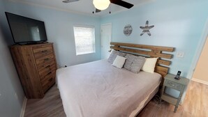 A bedroom with a bed, wooden dresser, TV, and a ceiling fan.