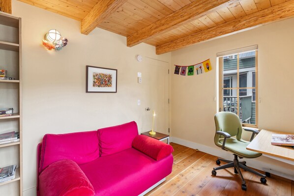 A room with a red sofa, a green office chair, a wooden ceiling, a framed picture, and a window with a view.