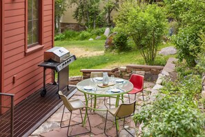 Une terrasse extérieure avec un barbecue, une table ronde et quatre chaises.