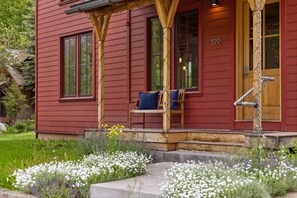 A red house with a porch, number 329, and a garden with white and purple flowers.