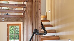 A wooden staircase with a modern design, a window with a view of greenery, and a light fixture on the wall.