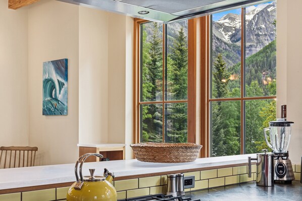 A kitchen with a large window, a kettle, a blender, and a woven basket on the counter.